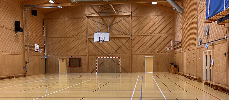 Sporthall med trägolv, träväggar, basketkorg, och mål.